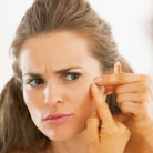 concerned woman looking at acne pimple on face