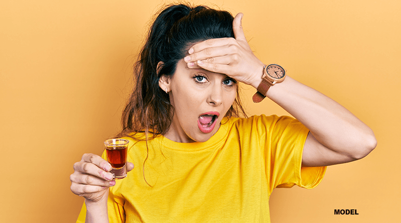 woman with shocked face while holding up hard alcohol shot