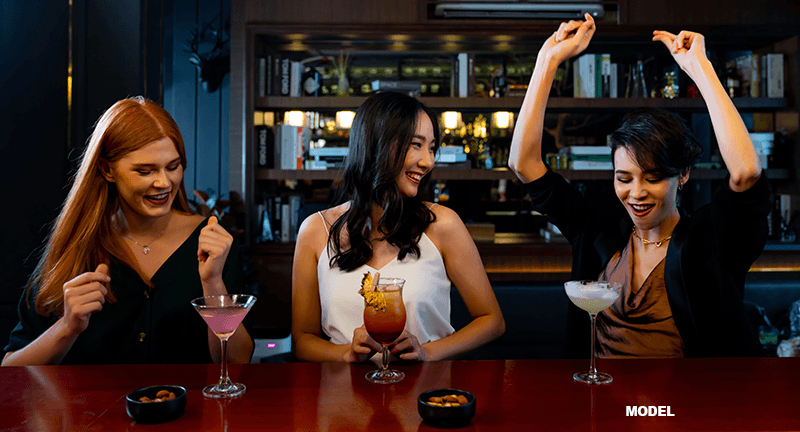 3 women friends partying in a bar with alcoholic drinks